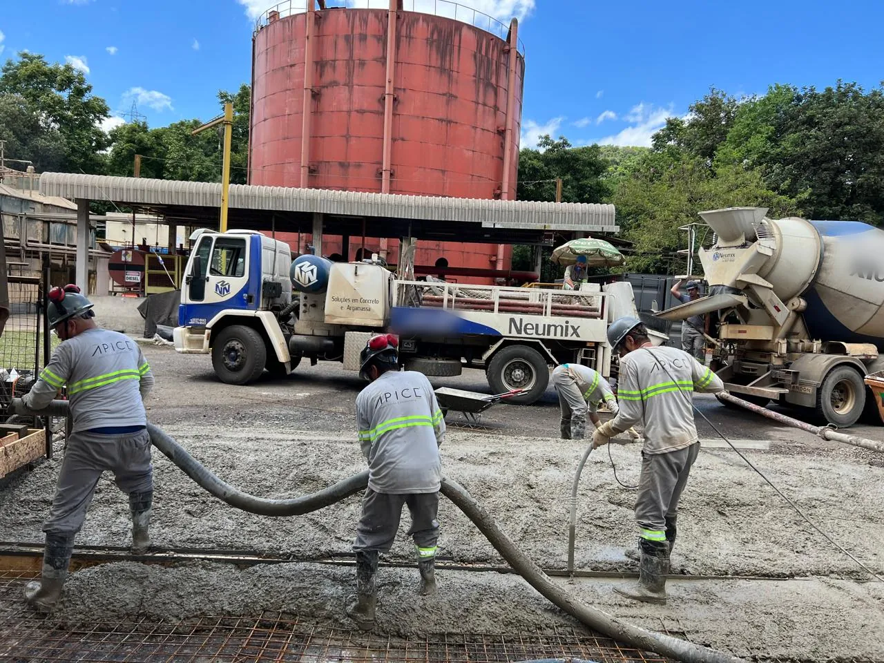 Equipe própria da Ápice, de uniforme e capacete, lança e adensa com vibrador o concreto bombeado sobre a tela soldada do pavimento de uma via industrial.