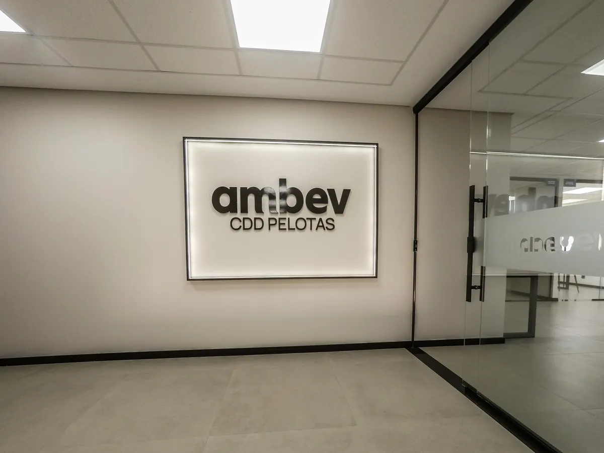 Hall de entrada entregue no CDD da Ambev em Pelotas, com painel retroiluminado, forro modular com LED, porcelanato e divisória de vidro jateado.