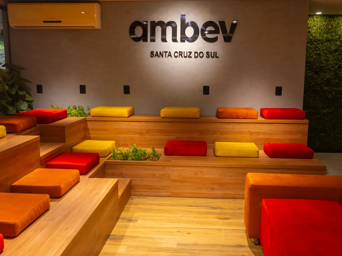 Arquibancada de madeira com almofadas coloridas e letreiro da Ambev Santa Cruz do Sul, em área de convivência entregue pela Ápice.